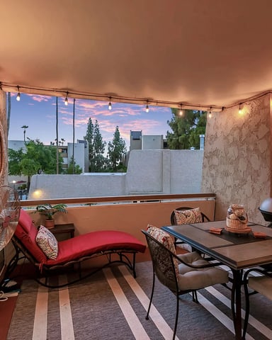 Rooftop patio with dining table, red chaise lounge, string lights, and city skyline view at dusk