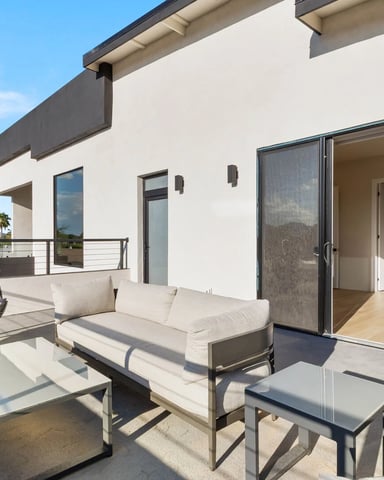 Modern white house with expansive patio featuring lounge seating, hanging chair, and sliding glass doors opening to interior spaces