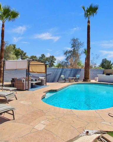 Backyard pool with turquoise water, lounge chairs, palm trees, and shaded seating area under pergola