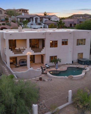 Modern white stucco house with pool and patio in desert hillside neighborhood at dusk