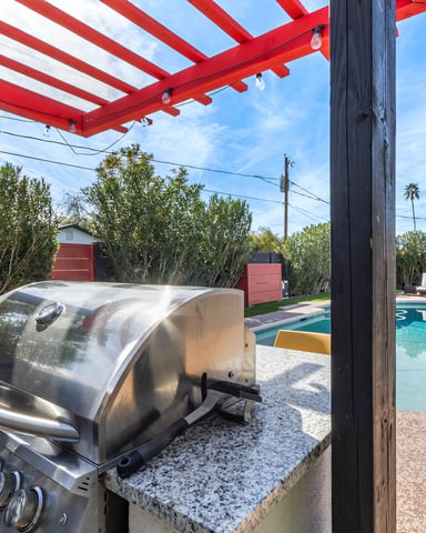 Backyard with red and white pergola, stainless steel grill, swimming pool, lounge chairs, and palm trees