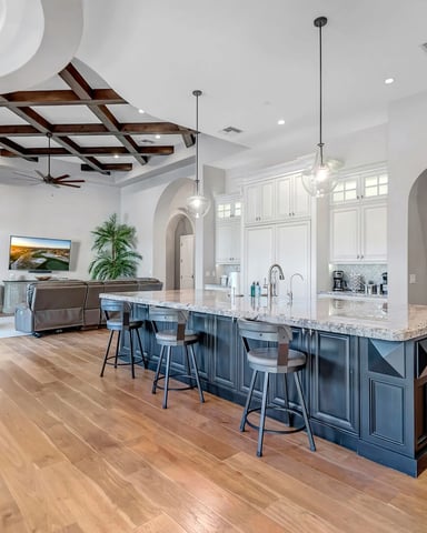 Open-plan kitchen and living room with large island, white cabinetry, dark wood ceiling beams, and hardwood floors