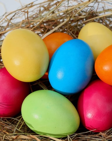 Colorful painted Easter eggs in yellow, orange, blue, green, and pink arranged in dried straw nest