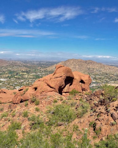 Desert hiking trail through red rock formations with valley and distant mountains under blue sky