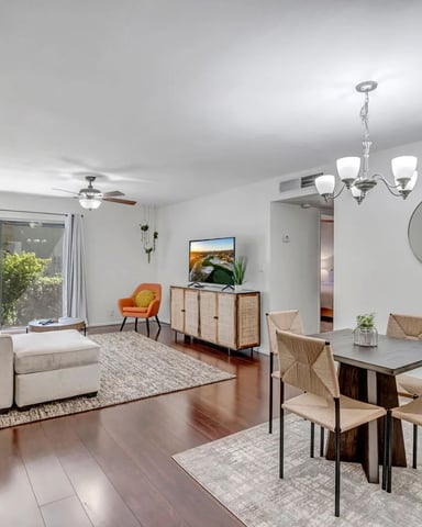 Open-plan living and dining room with cream sofa, dining table, teal chairs, and sliding glass doors to patio
