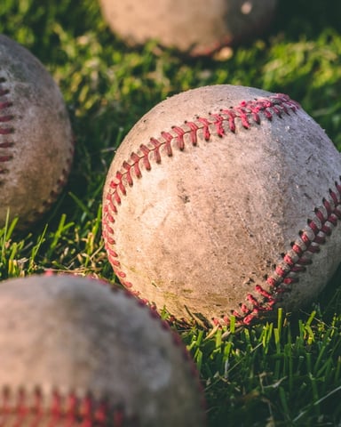 Three worn baseballs with red stitching on green grass