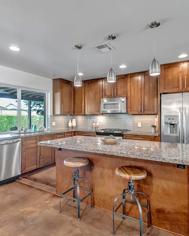 Modern kitchen with wood cabinetry, granite countertops, stainless steel appliances, island with bar seating, and pendant lighting