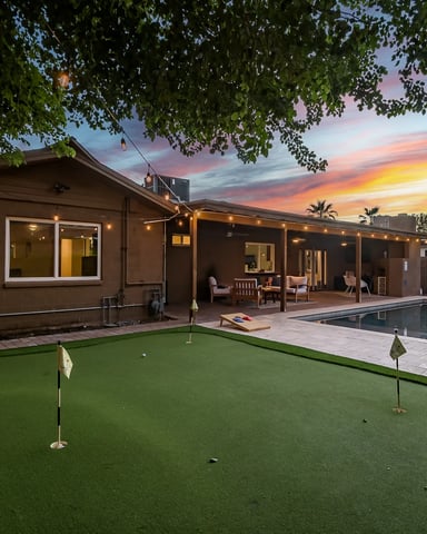 Modern backyard with putting green, pool, and brown house at sunset under tree canopy