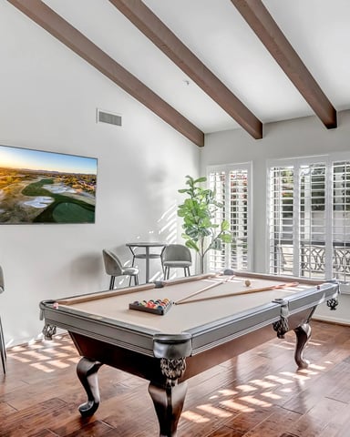 Game room with pool table, bar seating, exposed wood beams, white shutters, and golf course artwork on wall