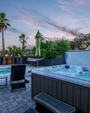 Backyard patio with hot tub, swimming pool, palm trees, and lounge chairs at dusk