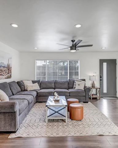 Modern living room with gray sectional sofa, ceiling fan, recessed lighting, and large sliding glass doors overlooking outdoor space