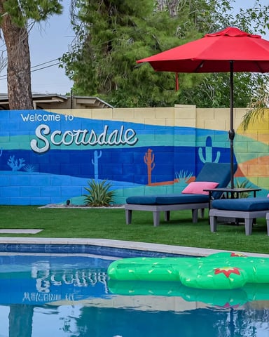 Backyard pool with green inflatable floats, lounge chairs, red umbrella, and colorful Scottsdale mural on wall