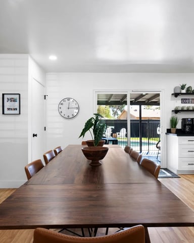 Open-plan kitchen and dining area with dark wood table, floral mural wall, white cabinetry, and glass doors to backyard