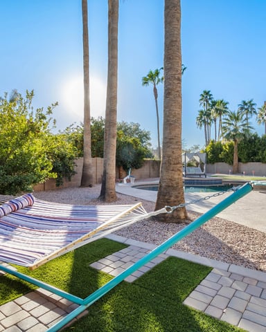 Backyard with striped hammock under tall palm trees, pool in background, patio with pergola and dining area