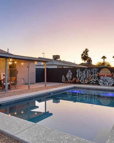Mid-century modern house with pool at dusk, string lights, cactus mural, desert landscaping, and palm trees