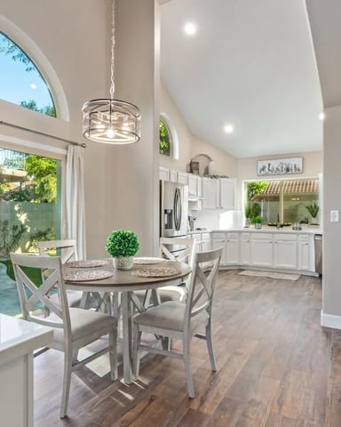Bright open-plan kitchen and dining area with round table, white cabinetry, stainless steel appliances, and arched windows overlooking patio.