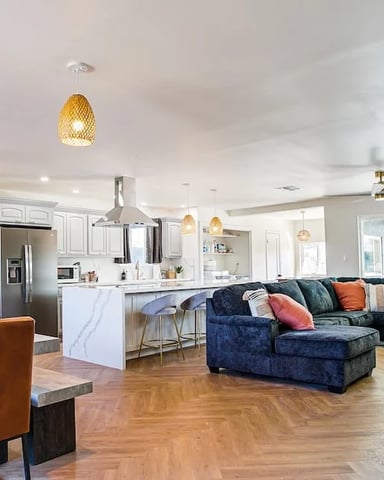 Open-plan living space with orange accent wall, dining table, navy sectional sofa, and modern kitchen with stainless steel appliances.