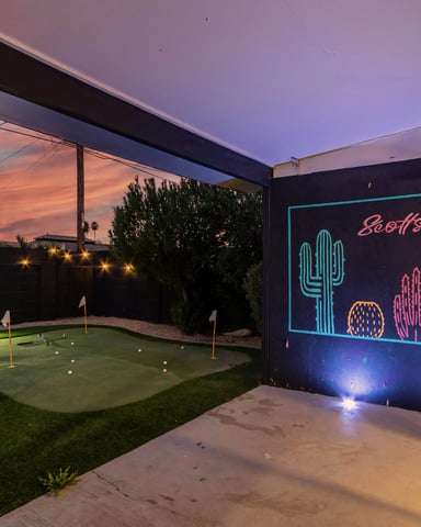 Backyard at dusk with neon cactus sign, mini golf course, lounge chairs, and sunset sky