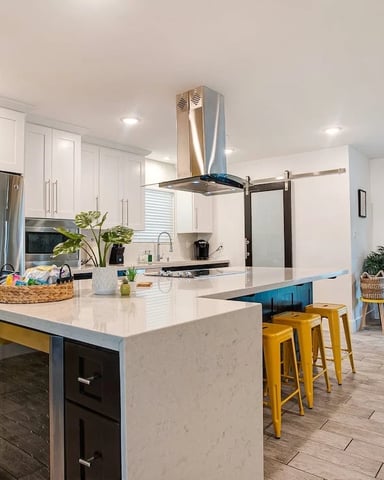 Modern kitchen with white cabinetry, stainless steel appliances, marble island with yellow bar stools, and open-plan living area with pool view.