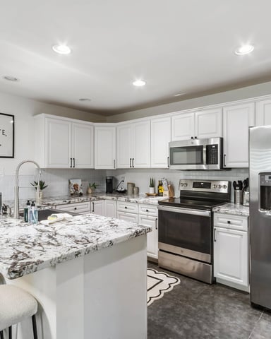 Modern kitchen with white cabinetry, granite countertops, stainless steel appliances, and island seating for two