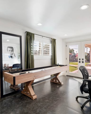 Recreation room with shuffleboard table, desk, and glass doors opening to backyard patio