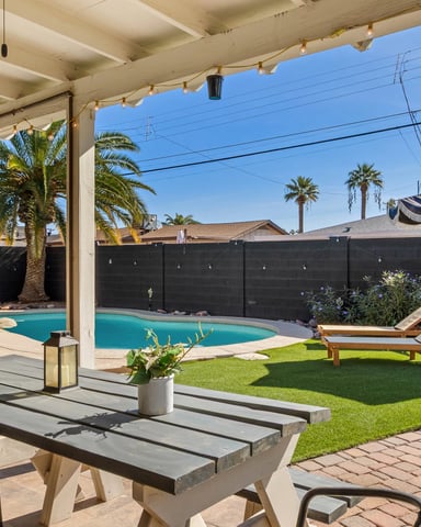 Backyard with swimming pool, covered patio, lounge chairs, palm trees, and black privacy fence