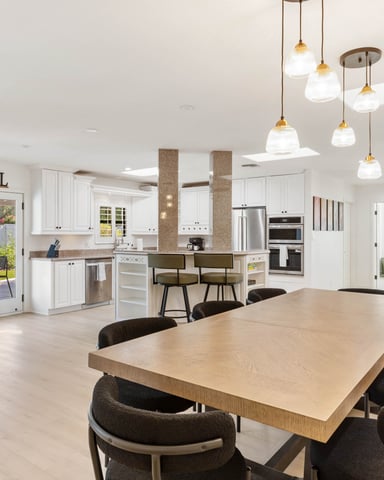 Open-plan kitchen and dining area with wood table, black chairs, white cabinetry, stainless steel appliances, and pendant lighting