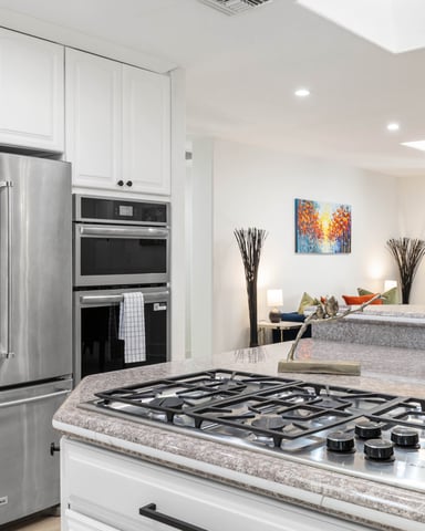 Modern kitchen with white cabinetry, stainless steel appliances, gas cooktop, and granite countertops opening to living area