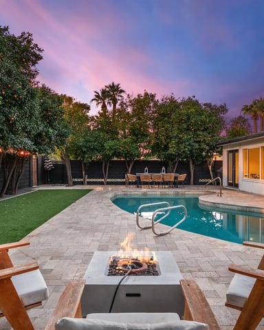 Backyard with swimming pool, fire pit, lounge chairs, and illuminated modern house at dusk