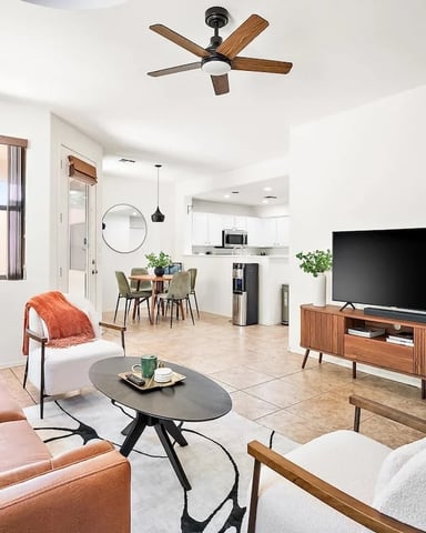 Open-plan living room with cognac leather sofa, TV on wood stand, dining area, and kitchen with ceiling fan