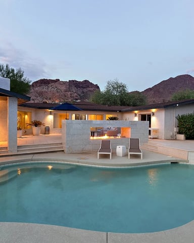 Modern desert home with illuminated pool, patio seating, and mountain backdrop at dusk