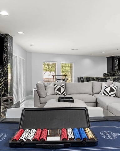 Modern recreation room with blue poker table, gray sectional sofa, black marble accent wall, and wall-mounted TV