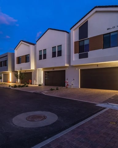 Row of modern white townhouses with garage doors lit at dusk, brick driveway and landscaping visible