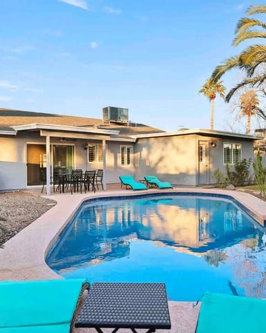 Single-story house with pool, patio lounge chairs, palm trees, and desert landscaping under clear blue sky