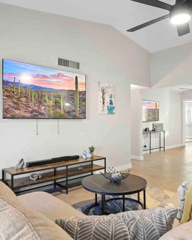 Living room with beige sectional sofa, TV mounted on wall, ceiling fan, and desert landscape artwork