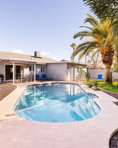 Single-story house with swimming pool, patio, palm trees, and desert landscaping under clear blue sky