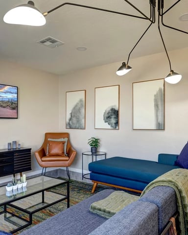 Modern living room with blue sofa, gray armchair, black media console, and multi-pendant ceiling lights