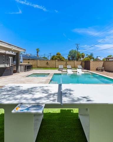 Backyard with turquoise swimming pool, ping pong table, lounge chairs, and modern house with covered patio