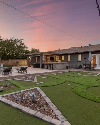 Modern home with backyard miniature golf course, pool, lounge chairs, and patio at dusk