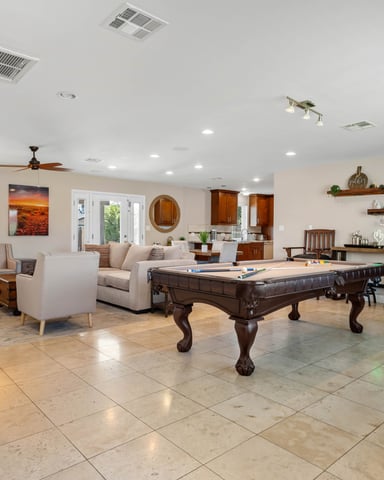 Large open recreation room with pool table, air hockey, seating area, and wooden shelving with decor