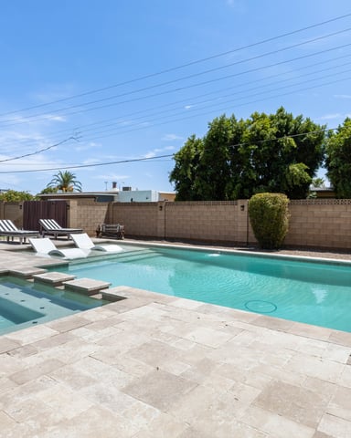 Backyard with turquoise swimming pool, spa tub, lounge chairs, and concrete patio surrounded by tan block wall