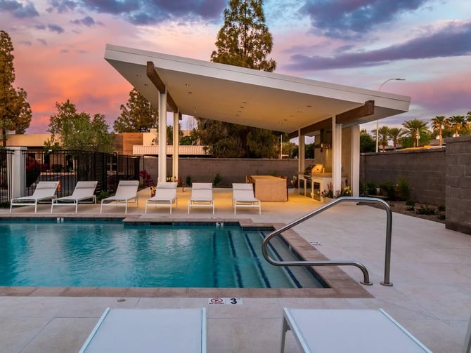 Modern pool area at sunset with lounge chairs, covered patio, and desert landscape at dusk