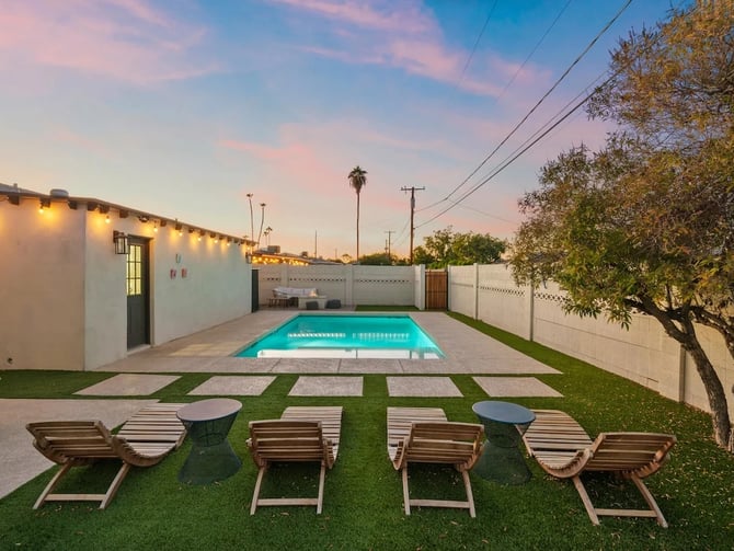 Backyard with illuminated mid-century modern house, rectangular pool, lounge chairs, and palm trees at dusk